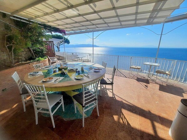An outdoor dining area with a table set for four, surrounded by white chairs, overlooking a scenic view of the sea.