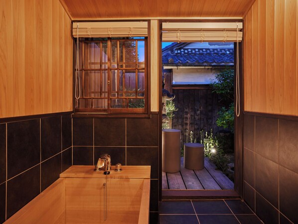 A traditional Japanese-style bathroom with a wooden bathtub, a window with sliding shoji screens, and a view of a wooden deck outside. - Nipponia Hotel Iga Ueno Jokamachi (Iga)