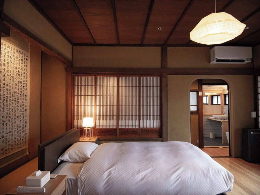 A traditional Japanese-style bedroom with a large bed, a wooden ceiling, and a sliding shoji screen door.