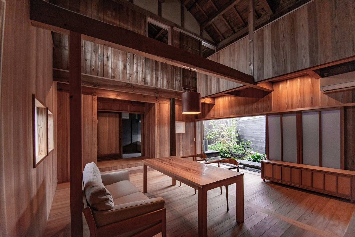 Une pièce spacieuse avec un plancher en bois, un canapé, une table à manger et une vue sur la verdure.