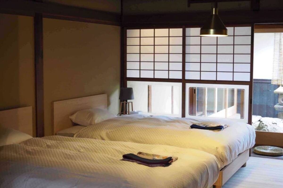 Une chambre de style japonais traditionnel, avec deux lits, un paravent en papier de riz (shoji) et une lampe suspendue.