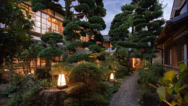 Ein traditioneller japanischer Garten mit Kieswegen, gepflegter Vegetation und Laternen.