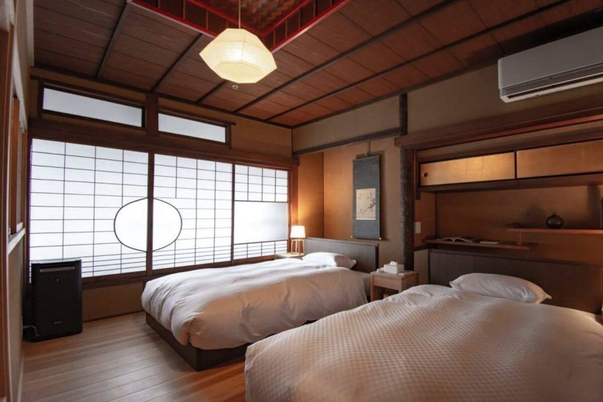 Une chambre de style japonais traditionnel, avec deux lits, un plafond en bois et une grande fenêtre dotée de panneaux coulissants en papier de riz (shoji).