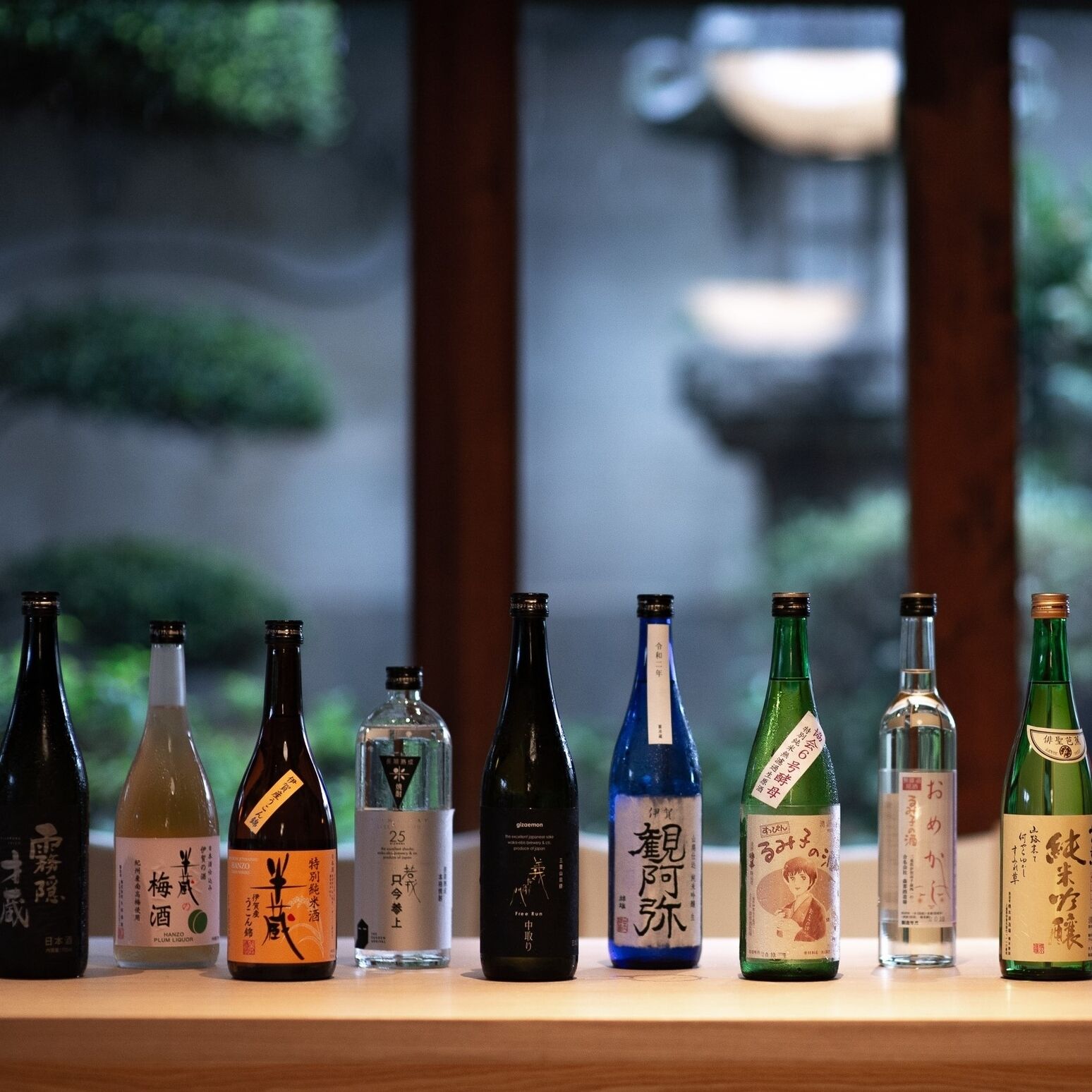 A row of various bottles on a shelf with a blurred outdoor background.