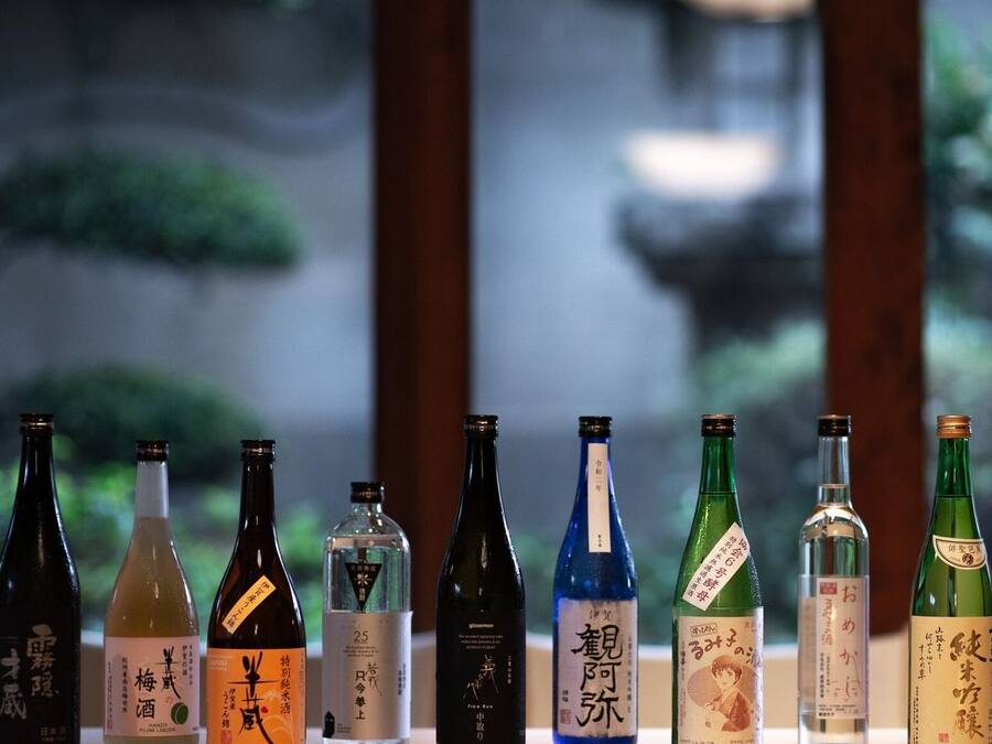 A row of various bottles on a shelf with a blurred outdoor background.