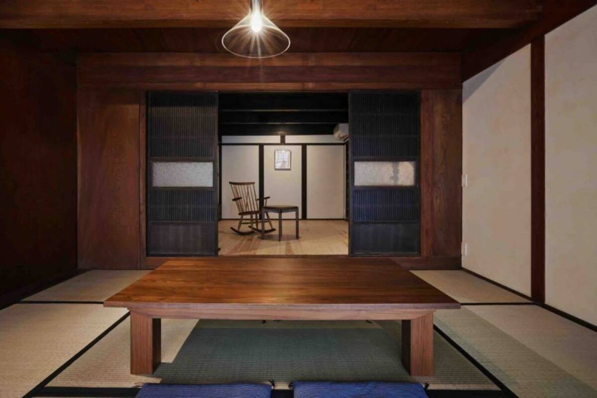 Une pièce de style japonais traditionnel, avec un sol recouvert de tatamis, une table en bois et une porte coulissante donnant sur une autre pièce.