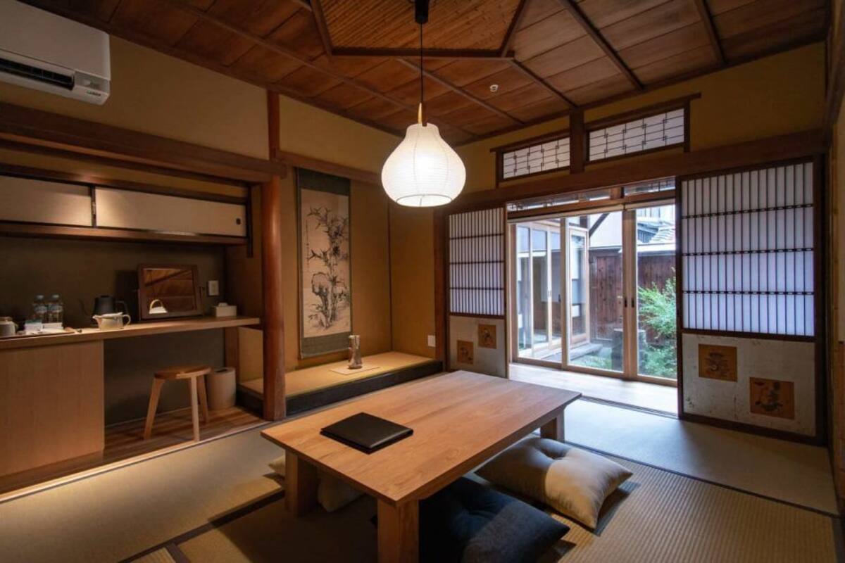 Une pièce de style japonais traditionnel, avec un sol recouvert de tatamis, une basse table en bois, un luminaire suspendu, des portes coulissantes en papier de riz (shoji) et une vue sur l’extérieur.
