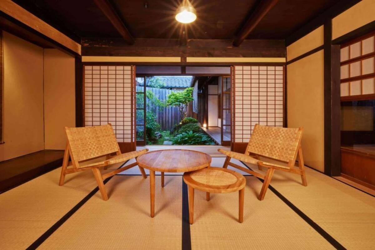 Une pièce de style japonais traditionnel, avec un sol recouvert de tatamis, une petite table et deux chaises, ainsi que des portes coulissantes donnant sur un jardin.