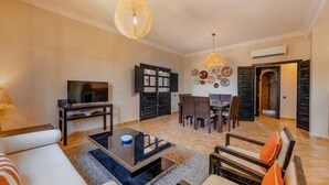 A living room with a TV, sofa, coffee table, and dining area. - Residence Dar Lamia Marrakech: 2 Bedroom Apartment (Dar Caïd Layadi)