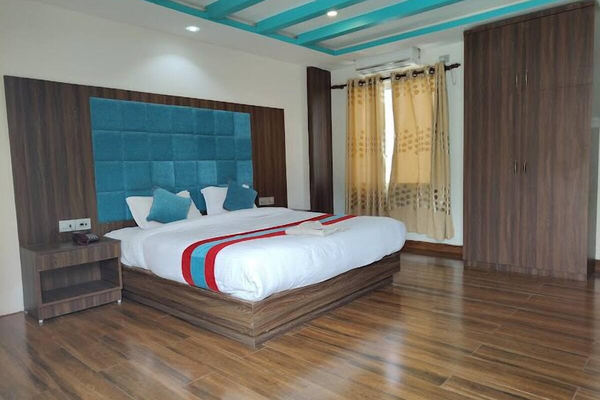 A bedroom with a large bed, wooden flooring, a blue headboard, and a wardrobe.