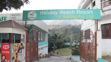 The entrance to Holiday Beach Resort & Rafting Pvt. Ltd. with a sign above the gate, potted plants, and a view of the surrounding greenery.