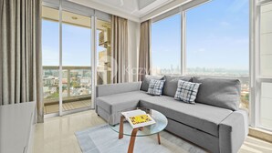 A modern living room with a grey sofa, a glass coffee table, and a view of a cityscape through large windows. - Canna by Kozystay - Menteng (Jakarta)