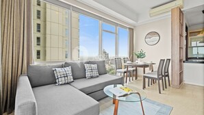 A modern living room with a grey sectional sofa, a glass coffee table, and a dining area with wooden chairs and a table. - Canna by Kozystay - Menteng (Jakarta)