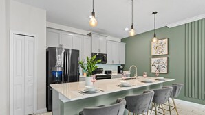 A modern kitchen with white cabinets, a large island with bar stools, and pendant lighting. - Chic 4BR Home with Mickey & Star Wars Rooms (Kissimmee)