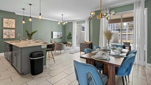 A modern kitchen with a central island, dining area with blue chairs, and a large window with curtains. - Chic 4BR Home with Mickey & Star Wars Rooms (Kissimmee)