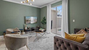 A living room with a sofa, armchair, and a coffee table. There is a TV mounted on the wall and a plant in the corner. - Chic 4BR Home with Mickey & Star Wars Rooms (Kissimmee)