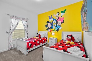 A children's room with two beds, each with Mickey Mouse-themed bedding, a Mickey Mouse plush toy on one bed, and a Mickey Mouse poster on the wall.