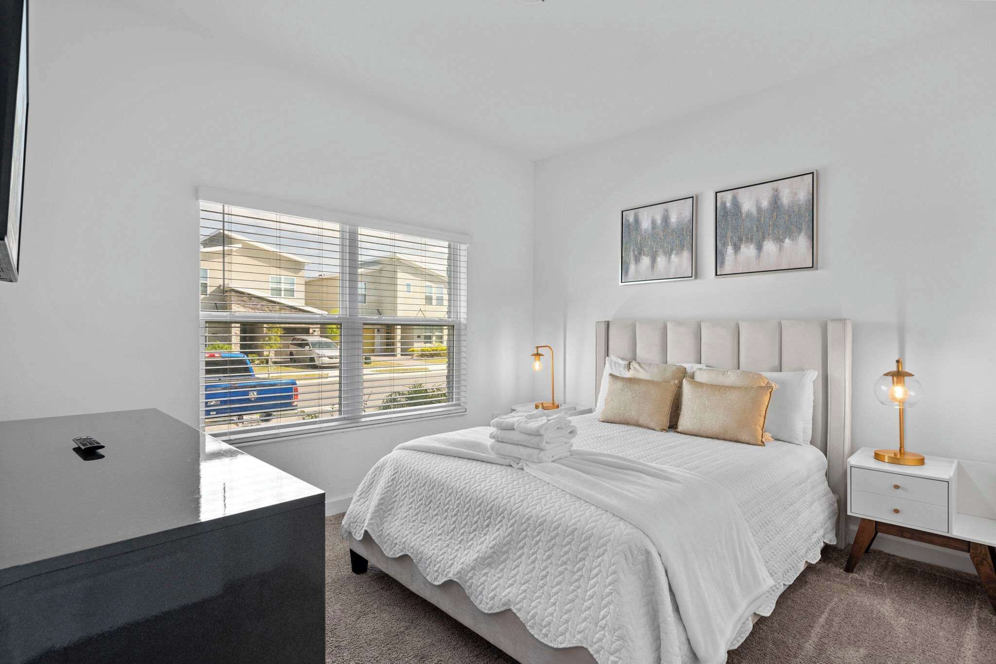 Une chambre à coucher comprenant un lit, des tables de chevet, un bureau et une fenêtre avec des stores.