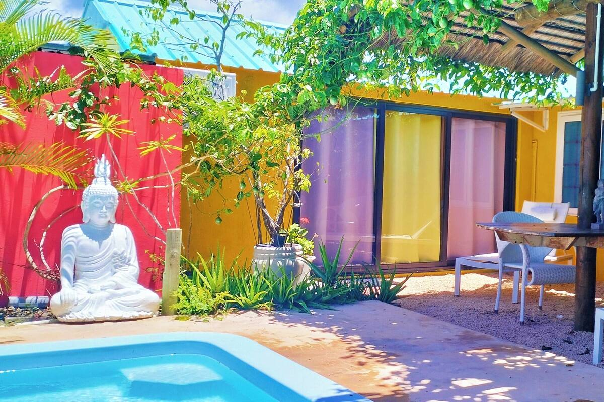 Un espace extérieur paisible, agrémenté d’une statue dédiée à la méditation, d’une petite piscine et d’une table à manger avec des chaises.
