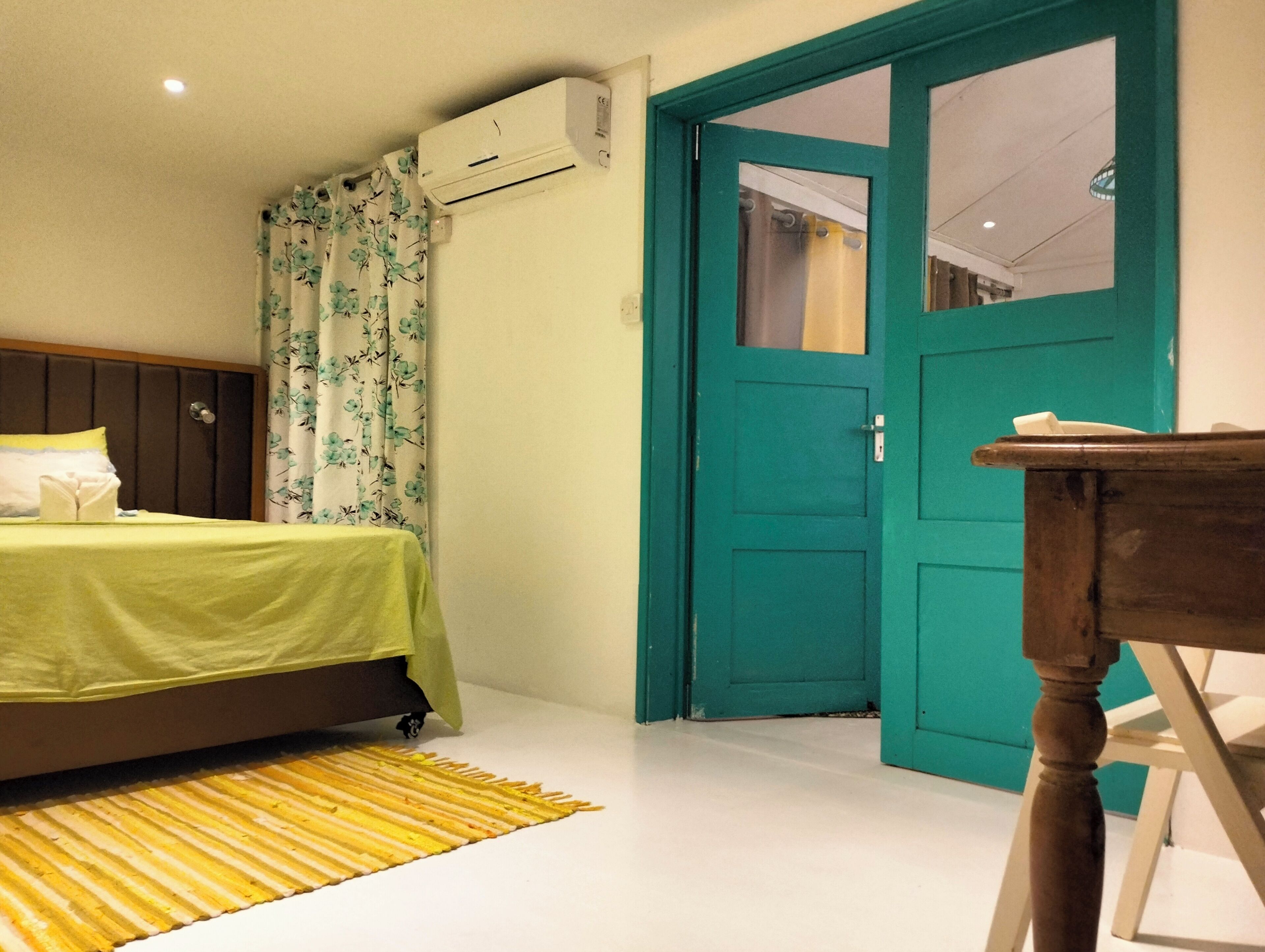 Quarto com uma cama, ar condicionado, porta verde-água e uma cadeira de madeira.