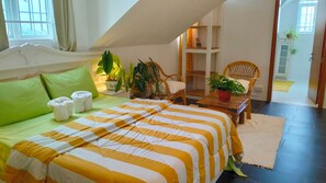 A bedroom with a bed, green pillows, a striped bedspread, a chair, a table with a plant, and a window.