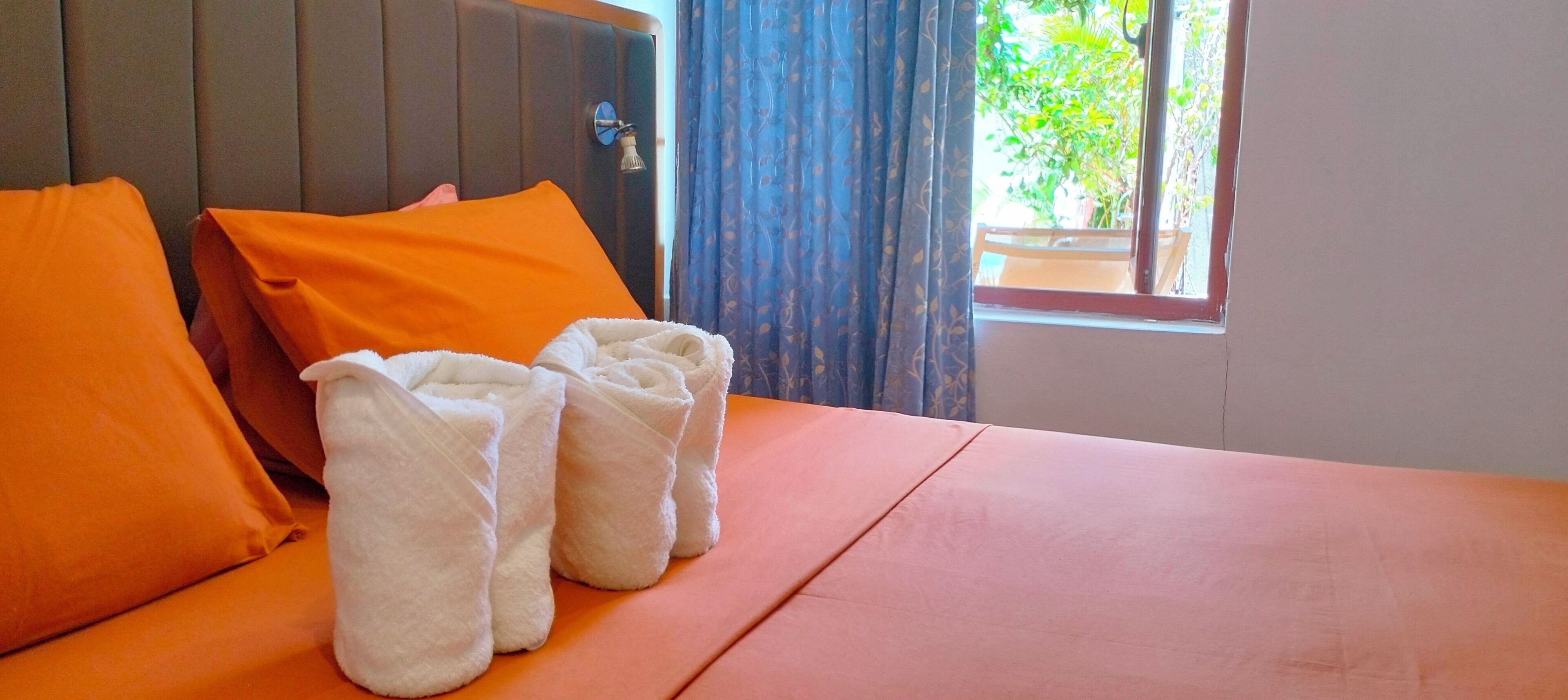 Una habitación de hotel con una cama, almohadas naranjas y dos toallas blancas.