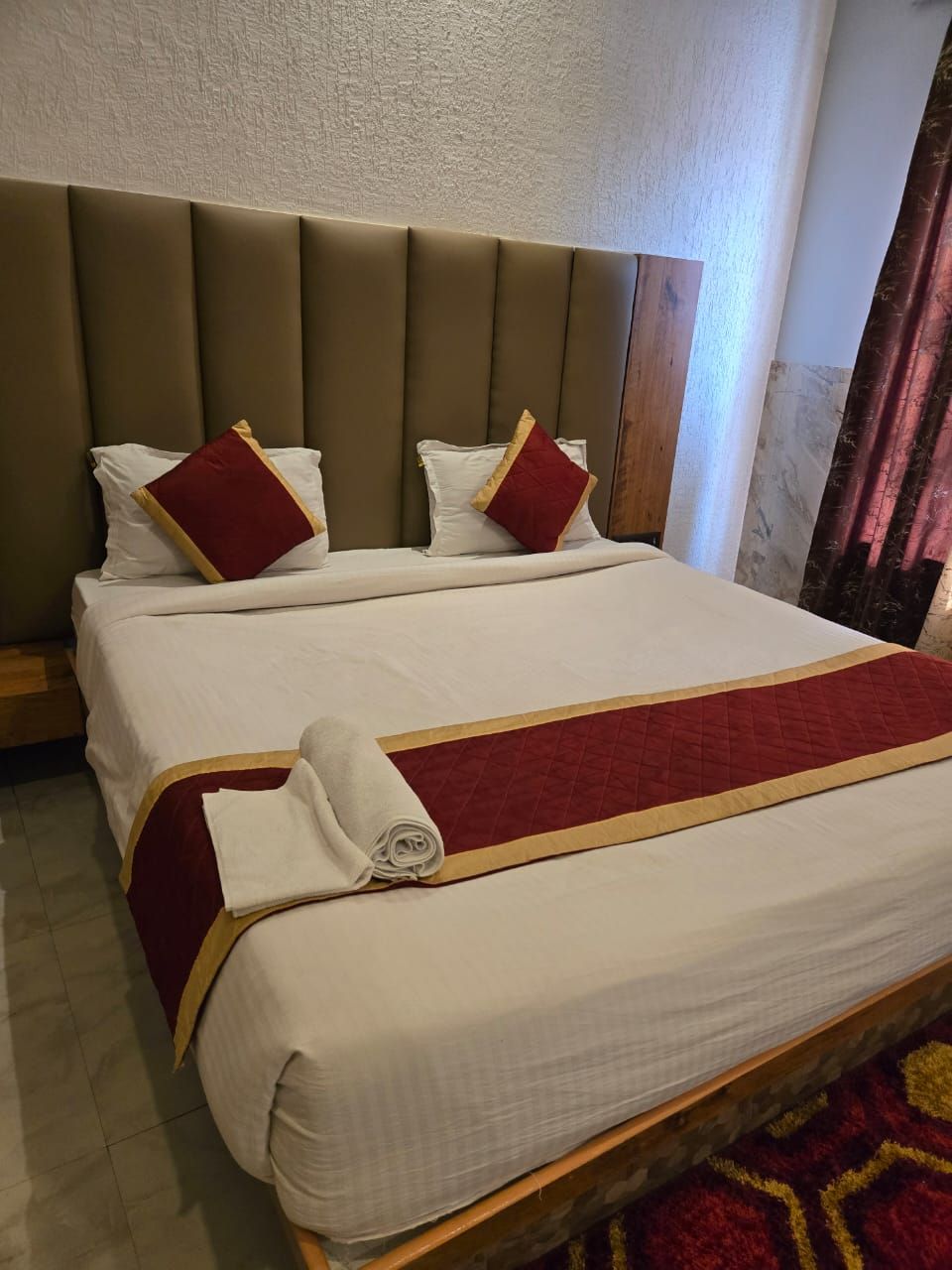 A hotel room with a large bed, a headboard, and a red and gold bedspread.