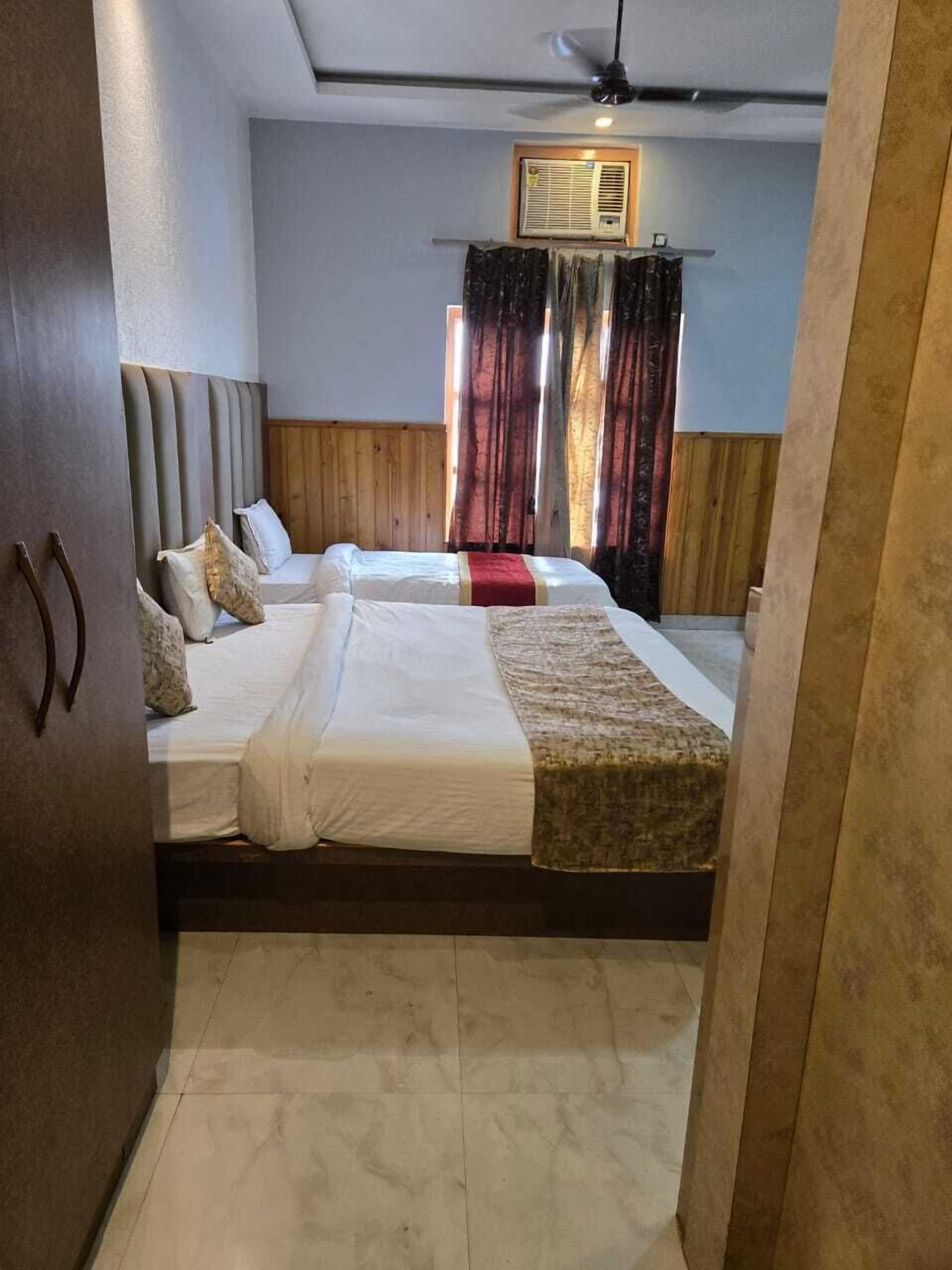 Habitación de hotel con dos camas, cabecera de madera, ventilador de techo y ventana con cortinas.