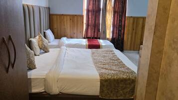 Habitación de hotel con dos camas, cabecera de madera, ventilador de techo y ventana con cortinas.