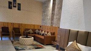 A hotel room with a large bed, a smaller bed, a sofa, a round ottoman, and a ceiling fan. - Avadh Sunshine Palace Hotel & Resort (Tarabganj)