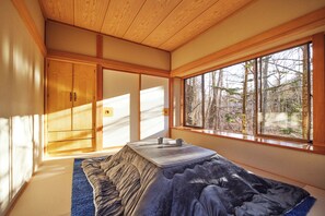 Experience serene tranquility in a traditional Japanese-inspired room with a tatami mat floor, low platform bed, and stunning forest views.