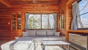 A log cabin interior with a sectional sofa, a dining table, and a built-in wood stove. - rinne 2nd living Kitakaruizawa Forest (Tsumagoi)