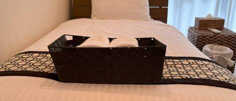 A neatly made bed with a white pillow and a brown headboard. A black woven basket is placed on the bed.