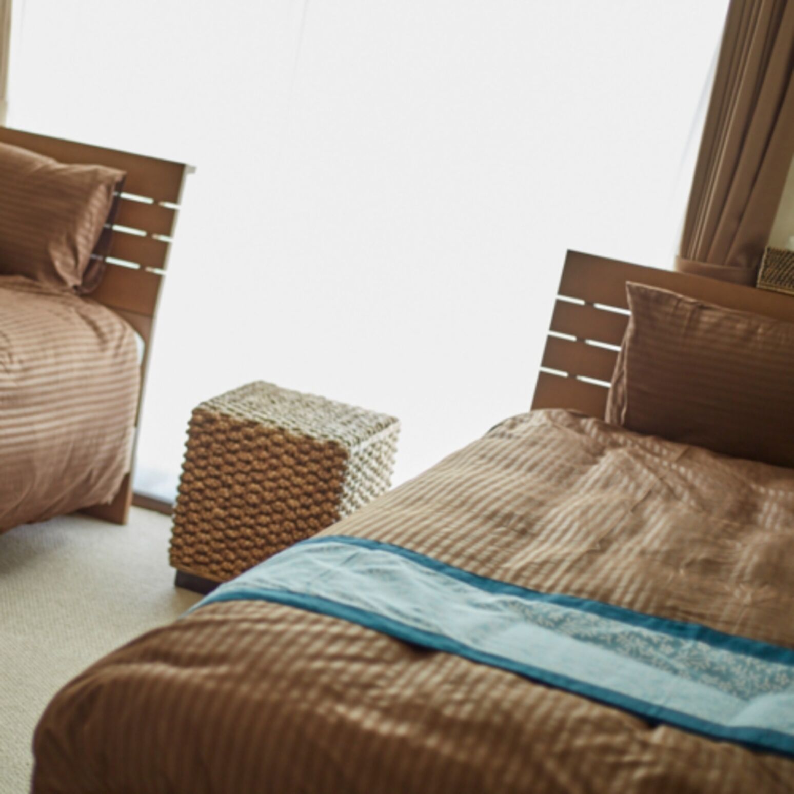 A bedroom with two beds, a small wooden stool, and a window with curtains.