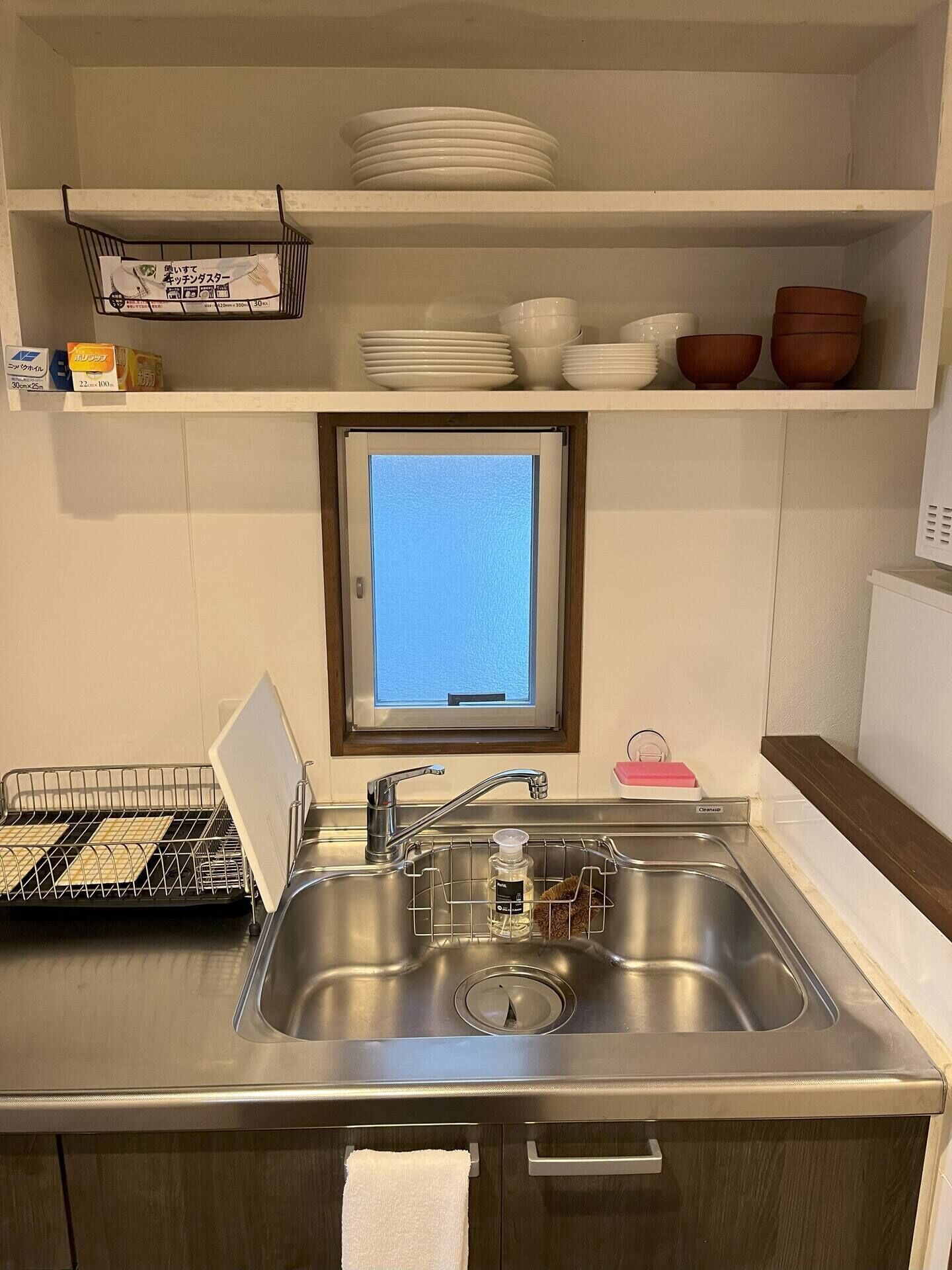 A kitchen with a stainless steel sink, a window with a view, and shelves with dishes and bowls.