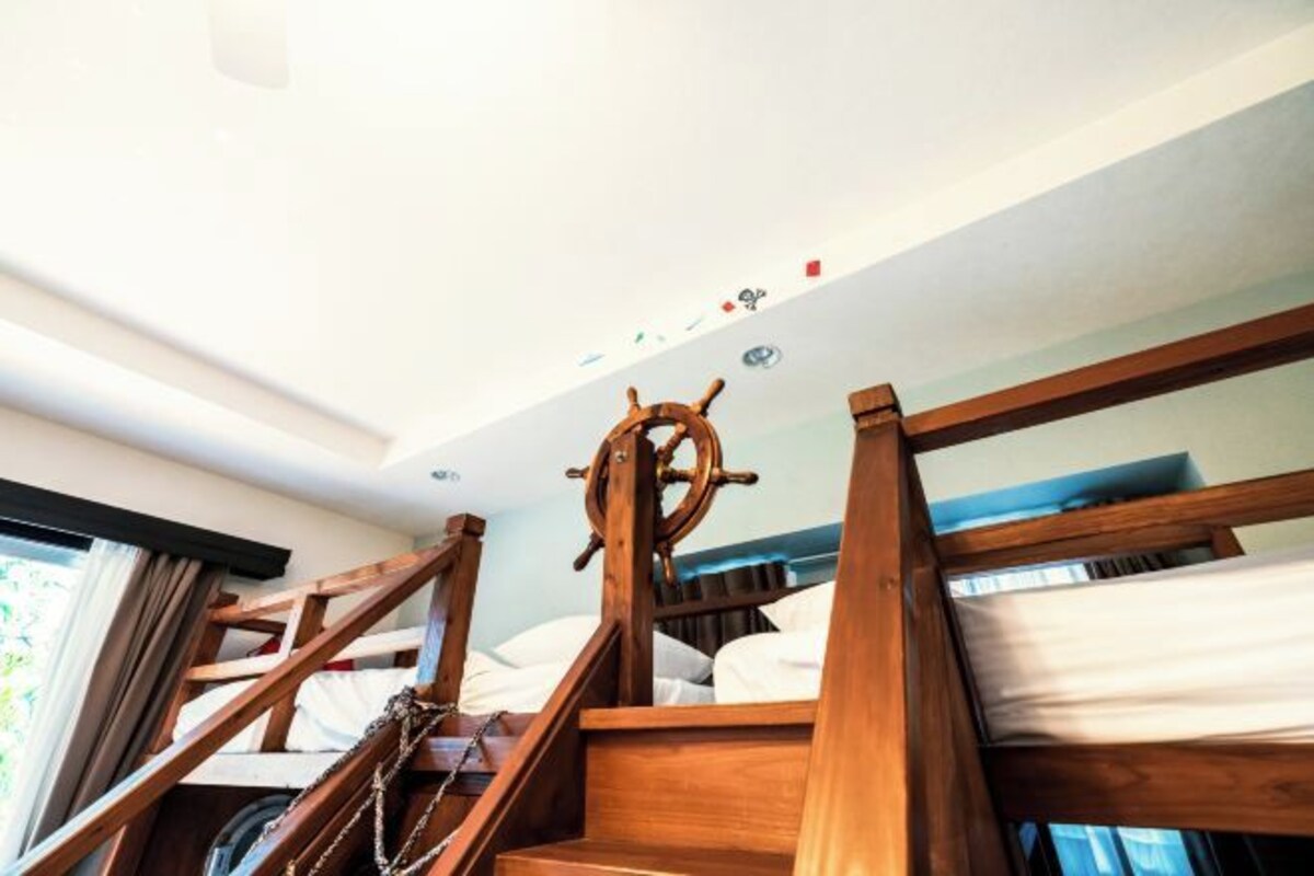 Una cama individual con dosel de madera con forma de timón, una ventana con cortinas y una lámpara en el techo.
