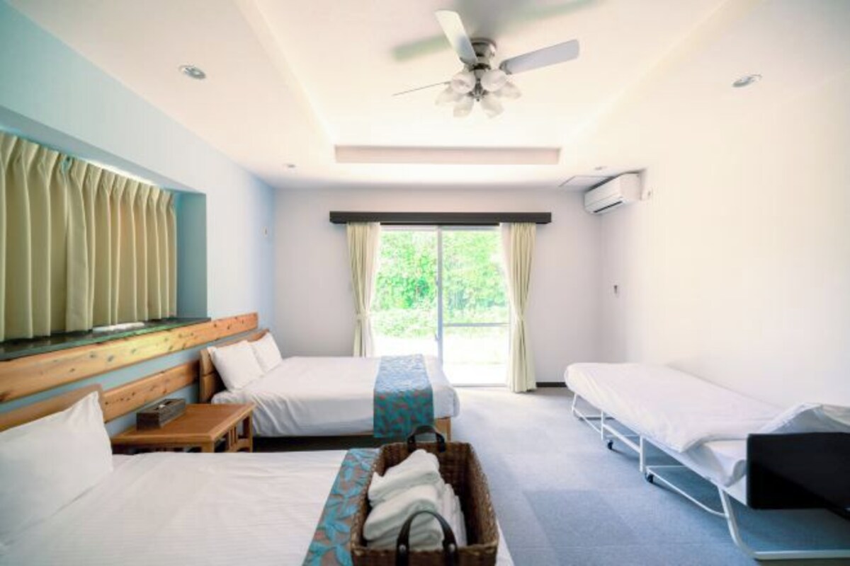 Habitación de hotel con dos camas, un ventilador de techo, una ventana con cortinas y una mesita.