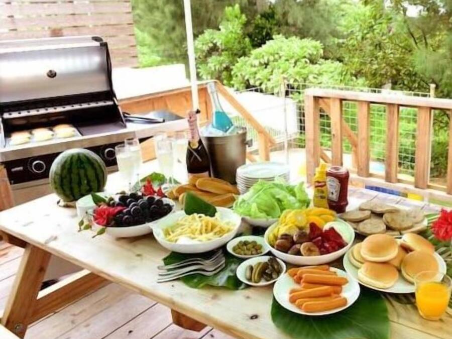 An outdoor dining area with a grill, various food items, and a bottle of champagne.