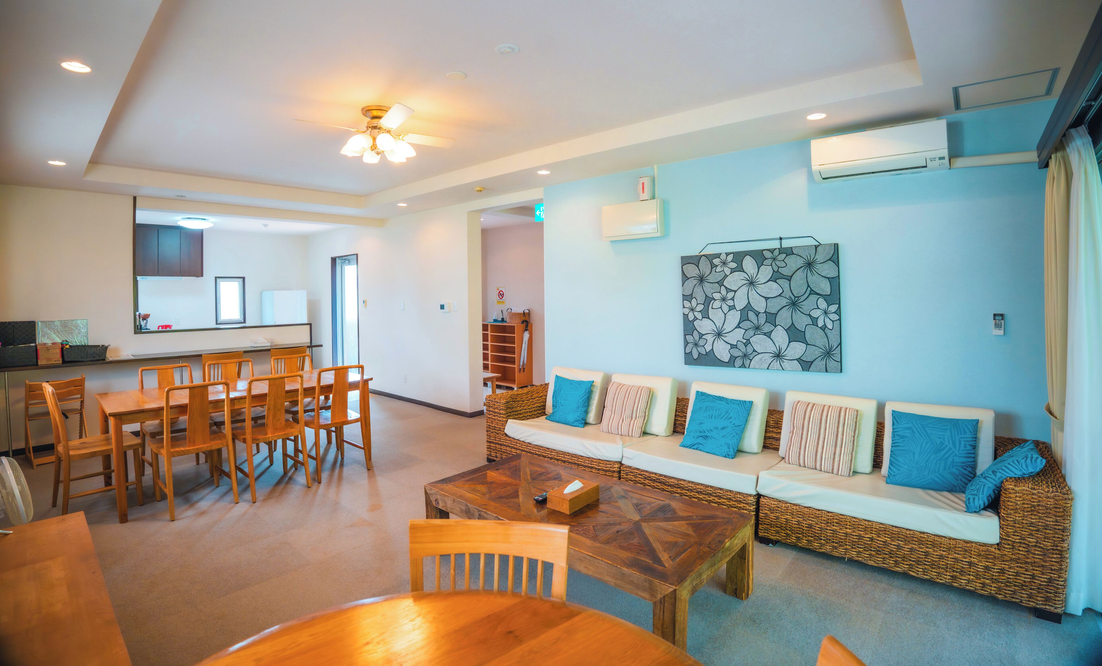 A spacious living area with a dining table, chairs, a sofa with cushions, a ceiling fan, and an air conditioning unit.