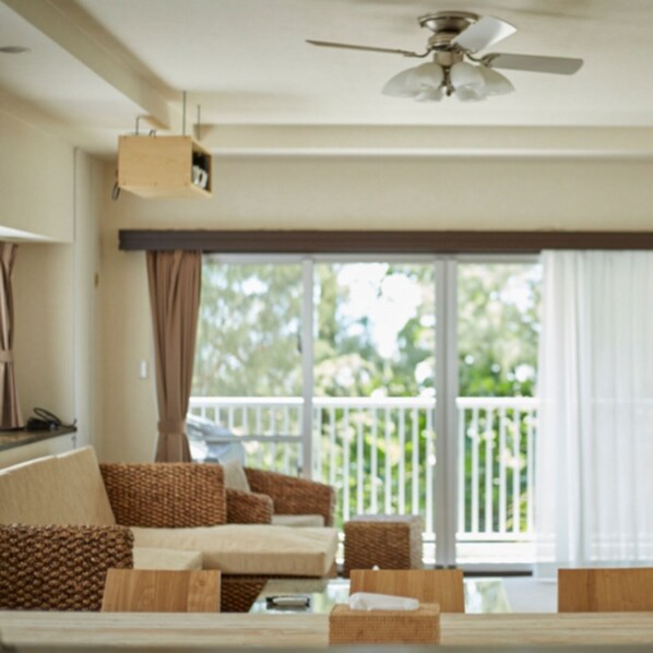 A room with a ceiling fan, a sofa, a table, and a view of a balcony.