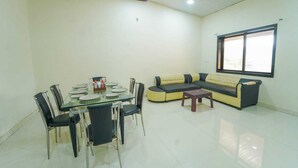 A spacious living area with a glass dining table, black chairs, a yellow and black sofa, and a small wooden table. - Lingmala Greens (Mahabaleshwar)