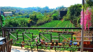 A balcony with a view of a lush green landscape, including terraced fields and distant buildings. - Lingmala Greens (Mahabaleshwar)