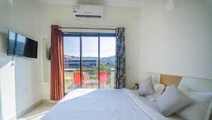 A hotel room with a bed, a flat-screen TV, a window with curtains, and a view of the outside. - Lingmala Greens (Mahabaleshwar)