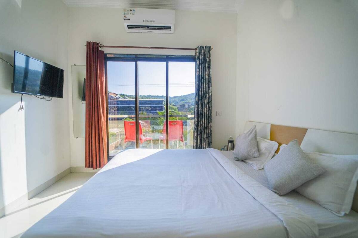 A hotel room with a bed, a flat-screen TV, a window with curtains, and a view of the outside.