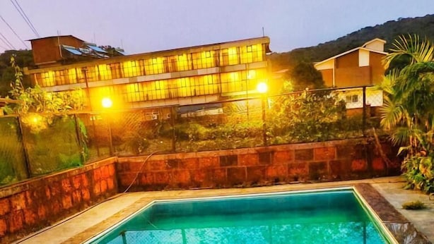 A rectangular swimming pool with a tiled edge, surrounded by a stone wall and a wooden deck. - Lingmala Greens (Mahabaleshwar)