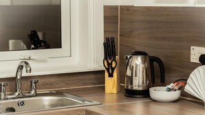 A modern kitchen with a stainless steel sink, a kettle, a knife block, and a bowl of snacks. - Kinnaird by Central Serviced Apartments (Dundee)