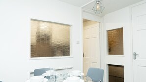 A dining area with a table set for four, a window with blinds, and a door leading to another room. - Kinnaird by Central Serviced Apartments (Dundee)