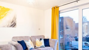 A modern living room with a grey sofa set, a large abstract painting, and a view of a residential area through a glass door. - Kinnaird by Central Serviced Apartments (Dundee)