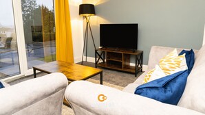 A living room with a sofa, a coffee table, a floor lamp, and a TV stand. - Kinnaird by Central Serviced Apartments (Dundee)