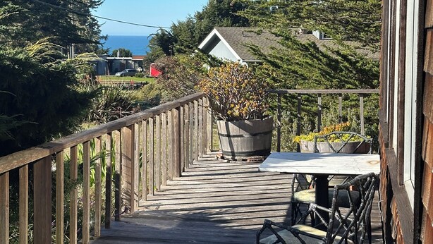 Une terrasse en bois avec une table et des chaises, donnant sur un quartier résidentiel avec des maisons et des arbres.